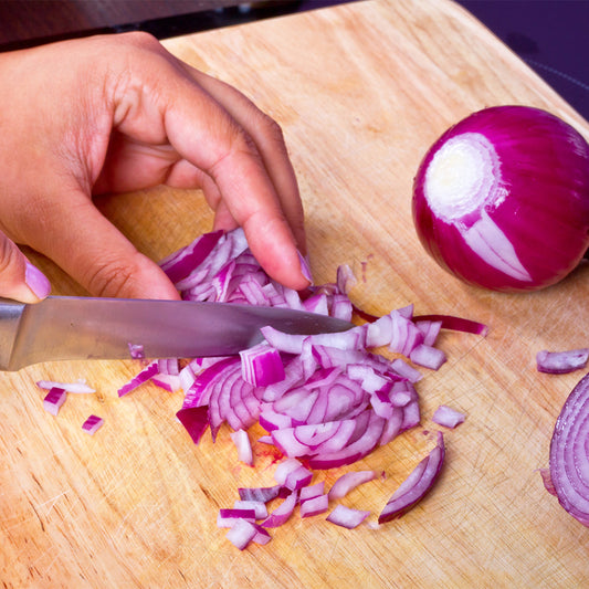 Hands with knife cutting red onion on cutting board