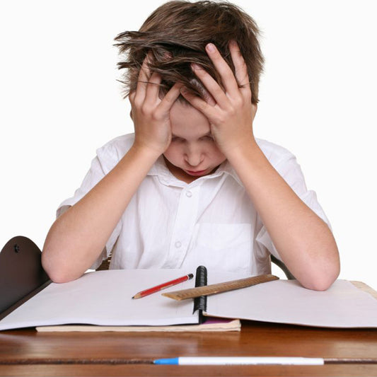 Boy with hands on head looking down at spiral notebook, pencil, rule, sitting at desk, with struggling face